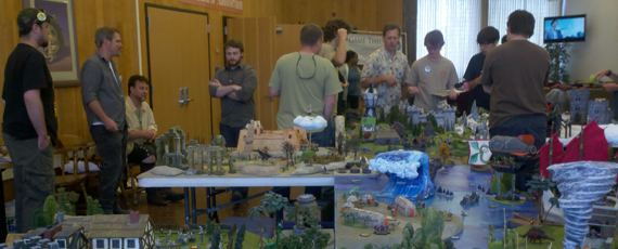 PolyCon attendees gather around a large table covered in miniature landscapes ranging from oceans, frozen tundra, humid jungles, and barren wastelands.
